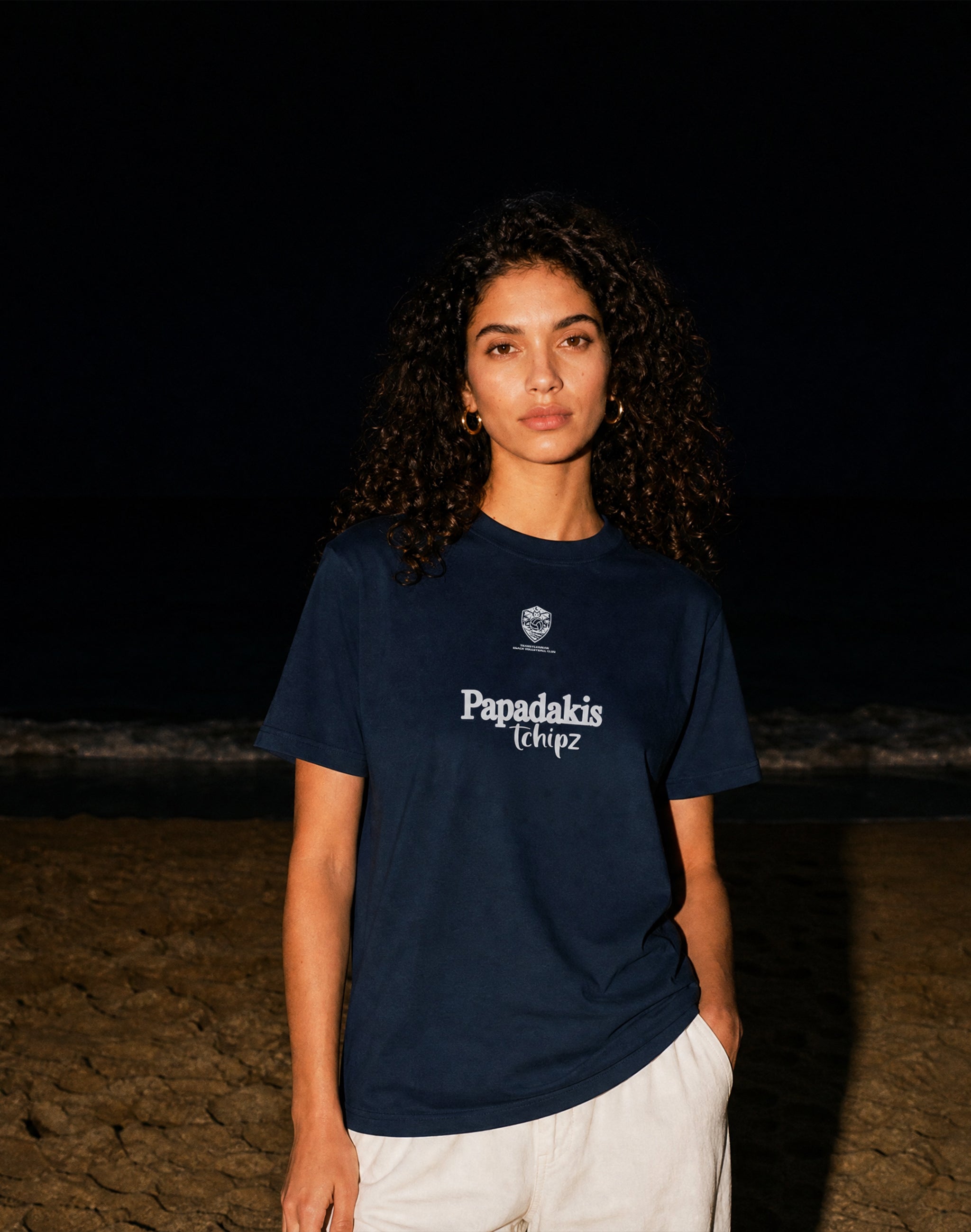 Transylvanian Beach Volleyball Club Tournament T-Shirt black sponsored by Papadakis Tchipz worn by female model flash photography on a beach at night — PERAMA Federations