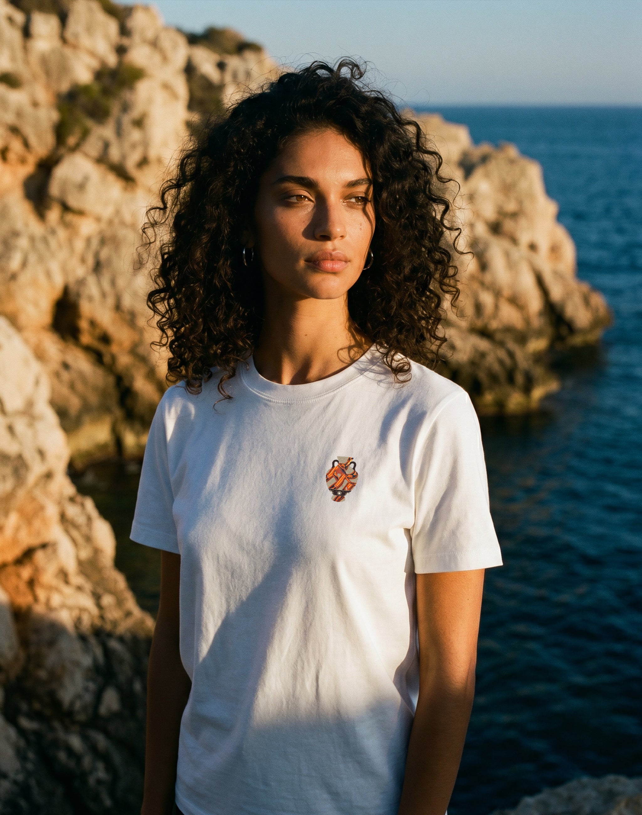 Amphora 03 white T-shirt worn by female model on Greek
coastline — PERAMA Odyssey