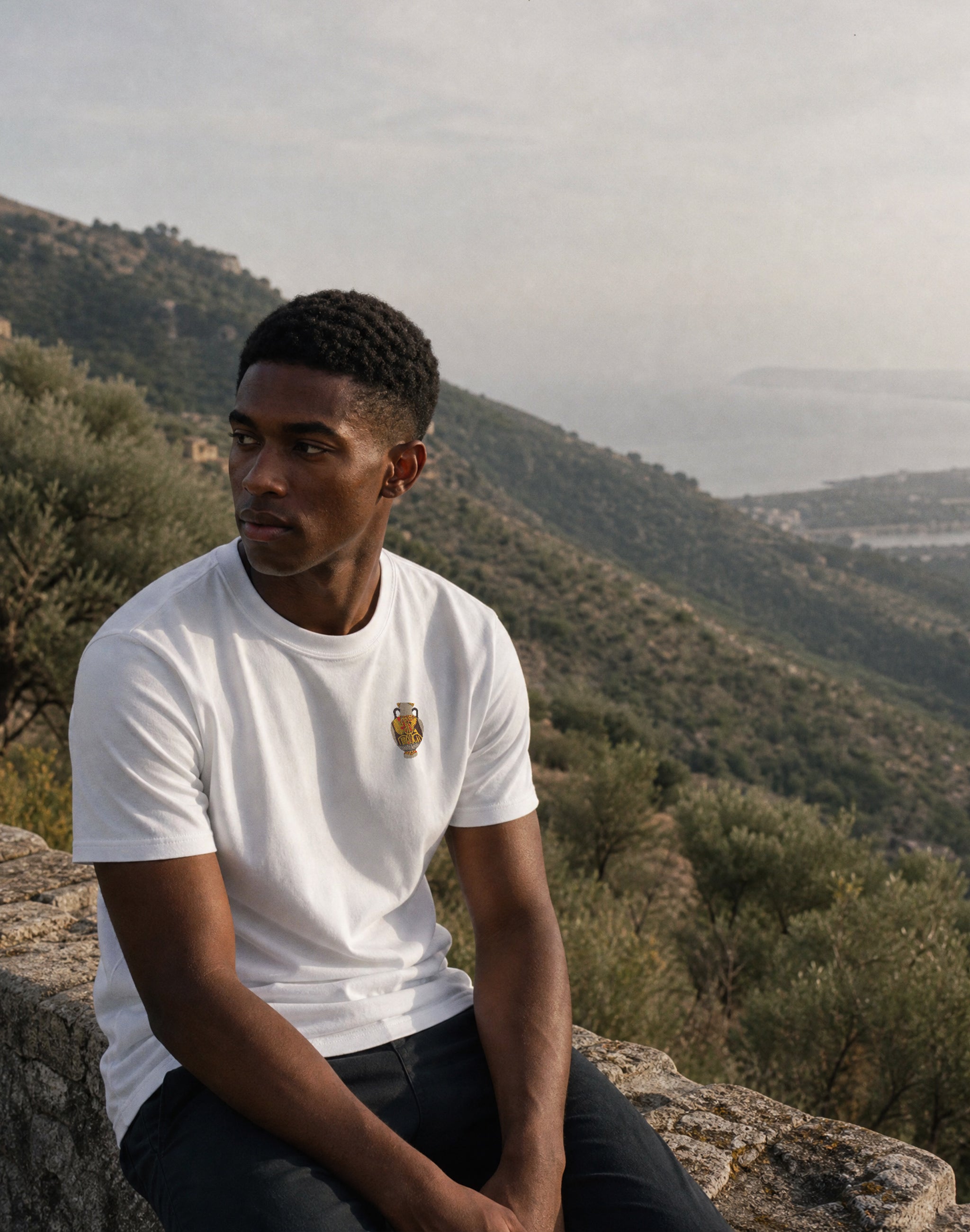 amphora-04-white-front worn by male model sitting on a wall in the greek mountains — PERAMA Classics