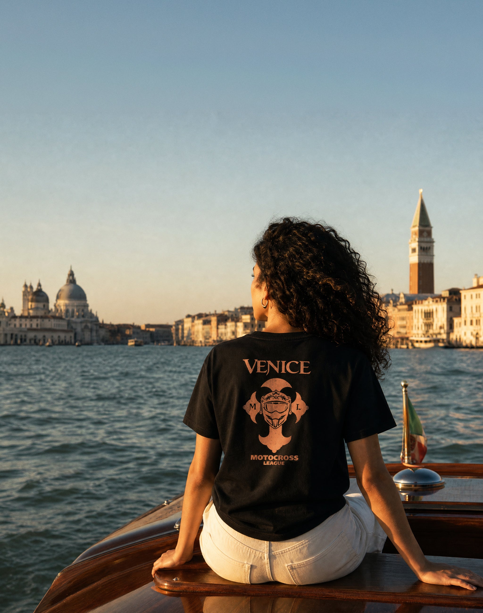 Venice Motocross League black t-shirt back print worn by female model on a boat in venice — PERAMA Federations